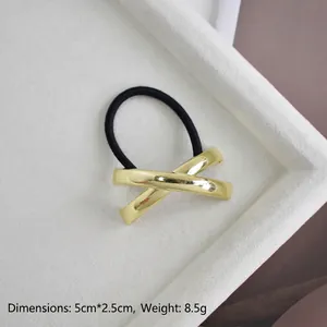 Detailed view of golden X-shaped alloy hair tie with high-elastic rope on white tray