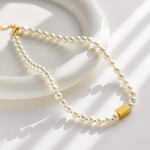 Close-up of pearl necklace with a rectangular gold pendant on a white ceramic tray