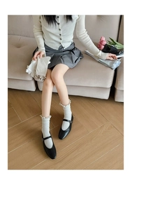 Detail of white knit crew socks with ruffled lettuce edge and black Mary Jane shoes