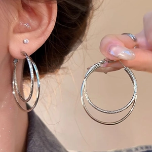 Detailed view of silver double hoop earrings with smooth and frosted texture on model