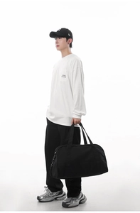 Asian male model carrying a large black travel duffel bag against a white studio background