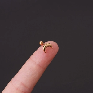 Macro shot of a tiny gold crescent moon cartilage stud earring held on a fingertip