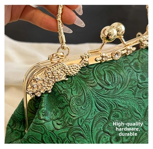 Macro detail of dark green floral embossed evening bag with gold phoenix rhinestone clasp