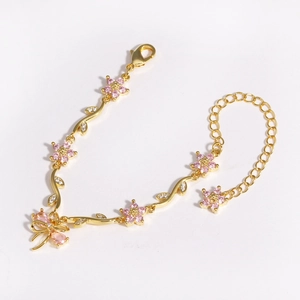 Detailed view of golden bracelet with pink flower accents and bow charm on white backdrop
