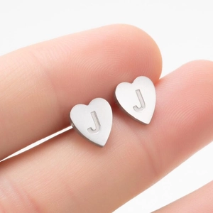 Gros plan d'une boucle d'oreille cœur en argent avec gravure lettre J entre les doigts