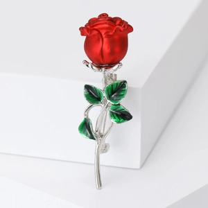 Elegant red rose brooch with green leaves and silver stem on a white platform