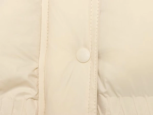Detailed macro view of cream-colored knit puffer jacket featuring a matte snap button