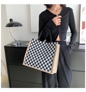 Close-up of checkerboard canvas and burlap tote bag held by model in minimalist setting