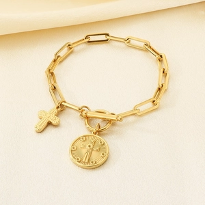 Gold OT clasp paperclip chain bracelet with cross and coin charms on silk background