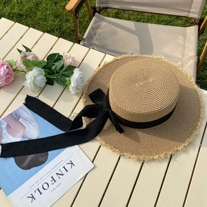 Close-up of flat-top straw hat featuring frayed edges and a black ribbon bow decoration