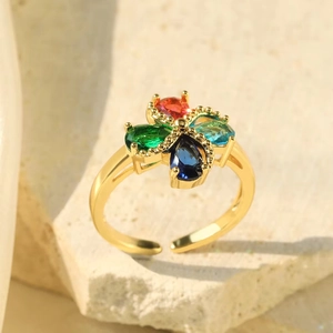 Macro shot of gold floral ring with red, green, and blue zircon gemstones on stone background
