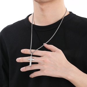 Close-up of a silver stainless steel cross pendant necklace worn by a male model