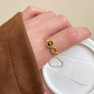 Detailed view of a gold-plated tiger eye ring on a hand holding a coffee lid