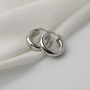 Detailed close-up of thick silver hoop earrings with S925 hallmark on silk background