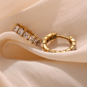 Détail de créoles plaquées or 18 carats avec zircons carrés sur du satin élégant