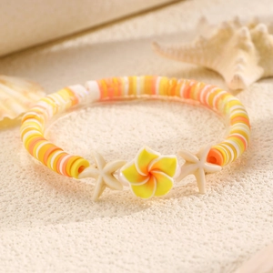 Dettaglio del bracciale da spiaggia con plumeria gialla e stelle marine su sabbia bianca