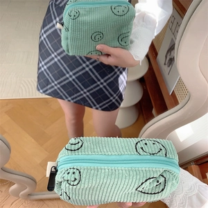 Mirror reflection showing a hand-held light green corduroy makeup bag with smiley faces