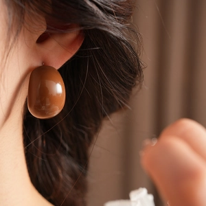 Close-up of model wearing large glossy brown resin bean-shaped drop earrings