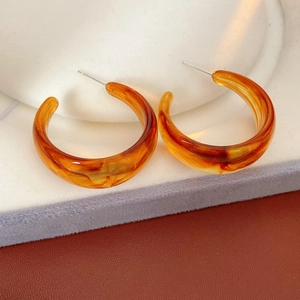 Macro detail of retro C-shaped resin amber earrings on a white velvet jewelry stand