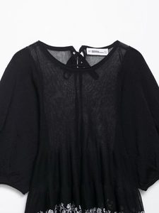 Detail of delicate white floral embroidery on a black knit linen blouse for women
