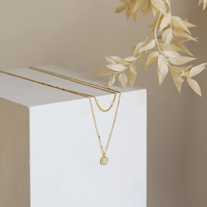 Double-layered gold necklace with round white mother-of-pearl pendant in minimalist style