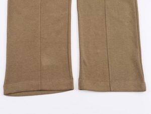 Detail of brown wide-leg knit trousers showing precise stitching and sharp center crease