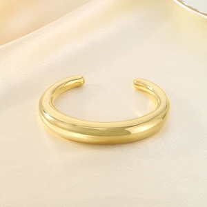 Vue détaillée d'un bracelet jonc ouvert en forme de C doré 18 carats sur de la soie beige