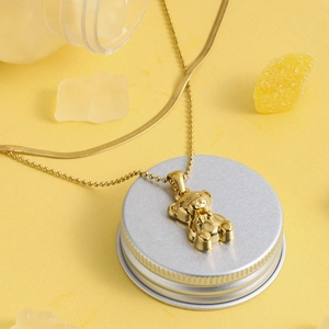 Detailed close-up of a 3D gold bear pendant with beaded and snake chain necklace on yellow base