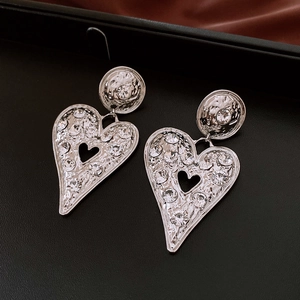 Macro shot of hammered silver heart earrings with sparkling rhinestones on black leather