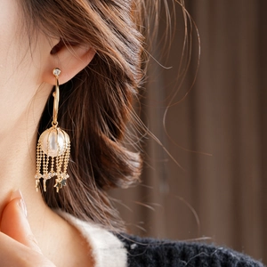 Gros plan de boucles d'oreilles étoile à pompon avec perle blanche et cage dorée