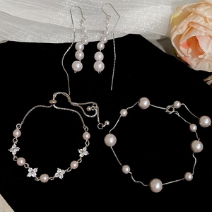 Detail of silver pearl jewelry set with clover charm on a black velvet background