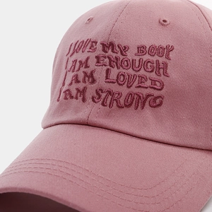 Macro detail of red positive quote embroidery on a dusty pink cotton baseball cap
