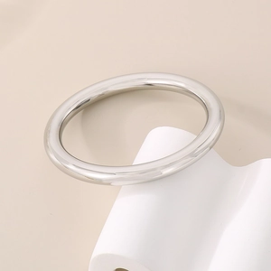 Close-up of polished silver titanium steel hollow bangle on white geometric background