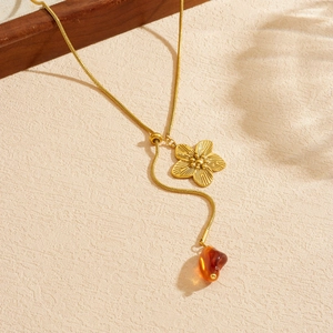 Gold camellia pendant necklace with amber resin charm on beige textured background