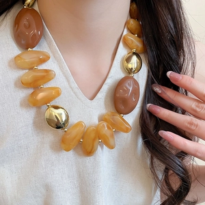 Detail of irregular amber and brown acrylic necklace beads with gold accents on model