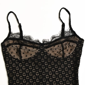 Dettaglio di canotta in pizzo nero con inserti in mesh a pois su sfondo bianco