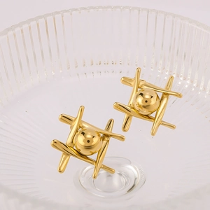 Detailed macro view of gold geometric cage earrings with smooth beads inside a glass bowl