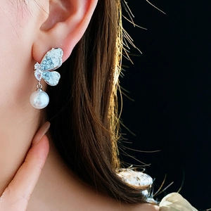 Close-up of butterfly earring with blue crystals and a white pearl on a model