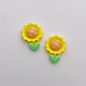 Detailed macro view of yellow resin sunflower charms with green leaves for DIY crafts