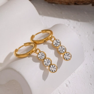 Close-up of gold hoop earrings with white and pink zircon pendants on a textured surface