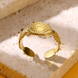 Close-up of golden stainless steel ring with sun relief on beige stone surface