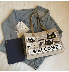 Flat lay of a beige cat tote bag with a blue denim jacket and lifestyle accessories