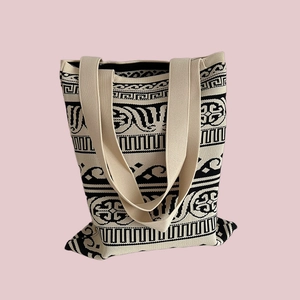 Close-up of beige woven canvas tote bag with black vintage geometric pattern on pink background