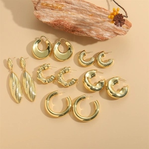 Golden minimalist earrings set featuring various textures and shapes on wooden stand