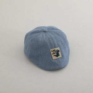 Dettaglio della coppola in denim azzurro per bambini con toppa a dinosauro e cuciture