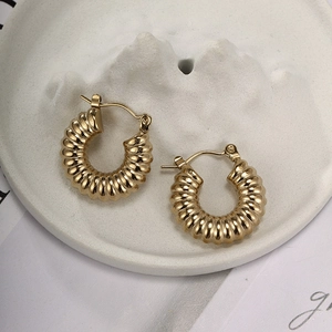 Close-up of golden chunky twisted hoop earrings on a minimalist white stone tray