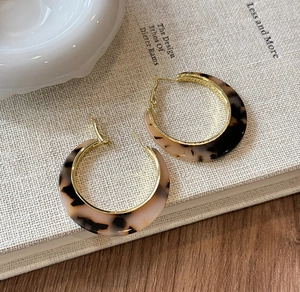 Detail of C-shaped leopard resin earrings with gold metal lining on a textured book