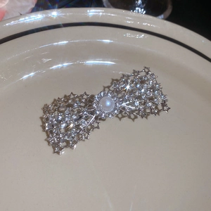 Detailed close-up of sparkling rhinestone bow hair clip with central pearl on ceramic plate