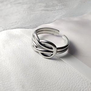 Detail of silver knot-shaped stainless steel open ring on white leather with ice prop