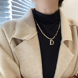 Détail d'un collier doré avec un pendentif lettre D incrusté de cristaux sur une chaîne à billes